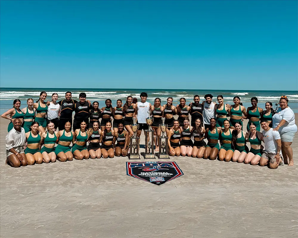 UT Dallas Power Dancers and Cheer team pose on the beach with their awards from competition.